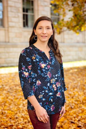 Melanie Seiler, Executive Director of Active Southern West Virginia, stands for a photograph in a floral shirt, the golden leaves of autumn carpeting the grown behind her.