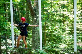 A WVU Tech student moves along an aerial ropes course surrounded by tree canopy.